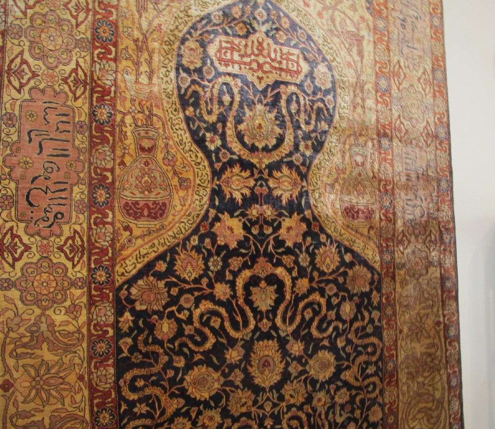 A mid-20th-century Turkish silk rug featuring a dark navy mihrab arch filled with floral motifs, surrounded by an ochre border with calligraphic script and bird illustrations. View XII