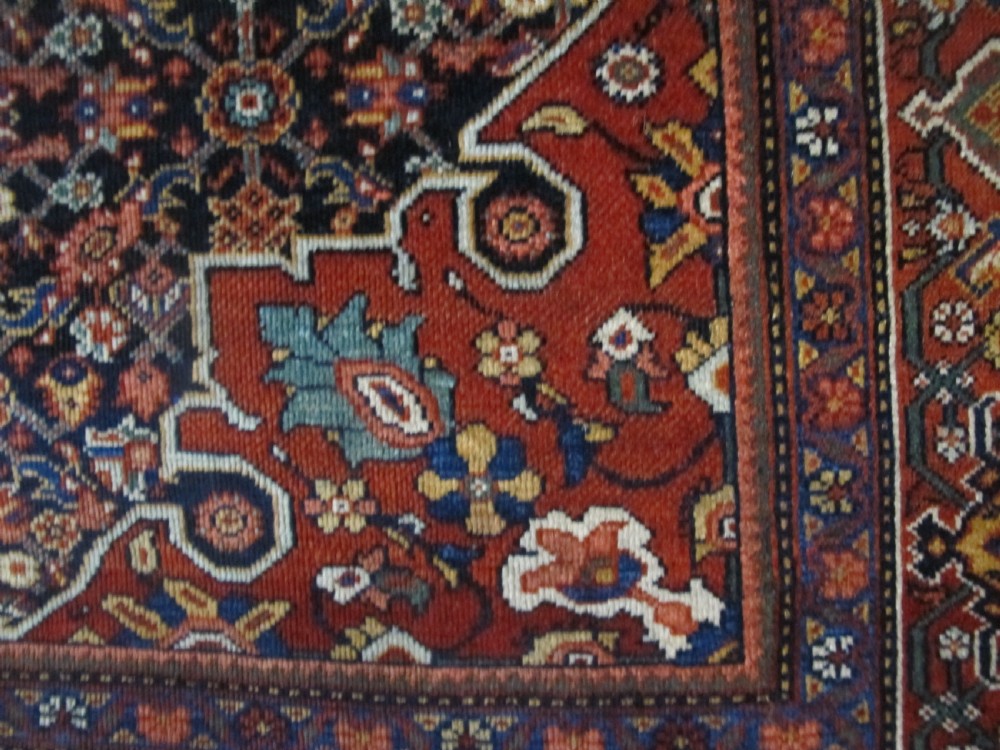 An antique hand-knotted Persian Fereghan wool rug featuring a central terracotta diamond medallion set within a dense navy blue floral field and ornate multi-layered borders. View V
