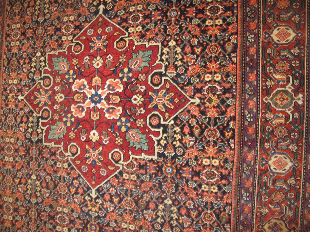 An antique hand-knotted Persian Fereghan wool rug featuring a central terracotta diamond medallion set within a dense navy blue floral field and ornate multi-layered borders. View IX