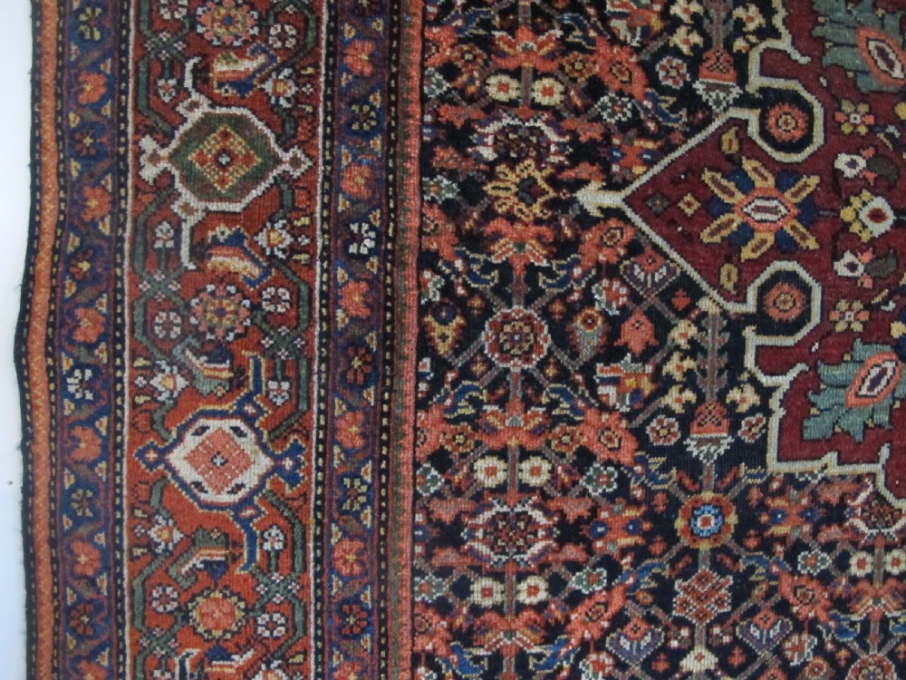 An antique hand-knotted Persian Fereghan wool rug featuring a central terracotta diamond medallion set within a dense navy blue floral field and ornate multi-layered borders. View X