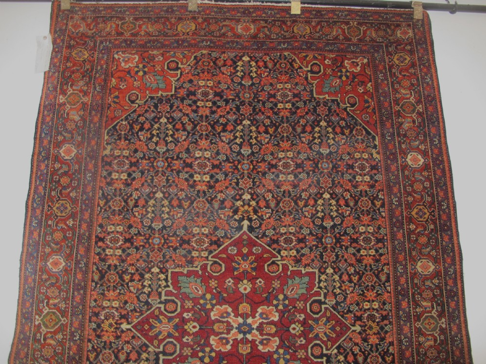 An antique hand-knotted Persian Fereghan wool rug featuring a central terracotta diamond medallion set within a dense navy blue floral field and ornate multi-layered borders. View XI