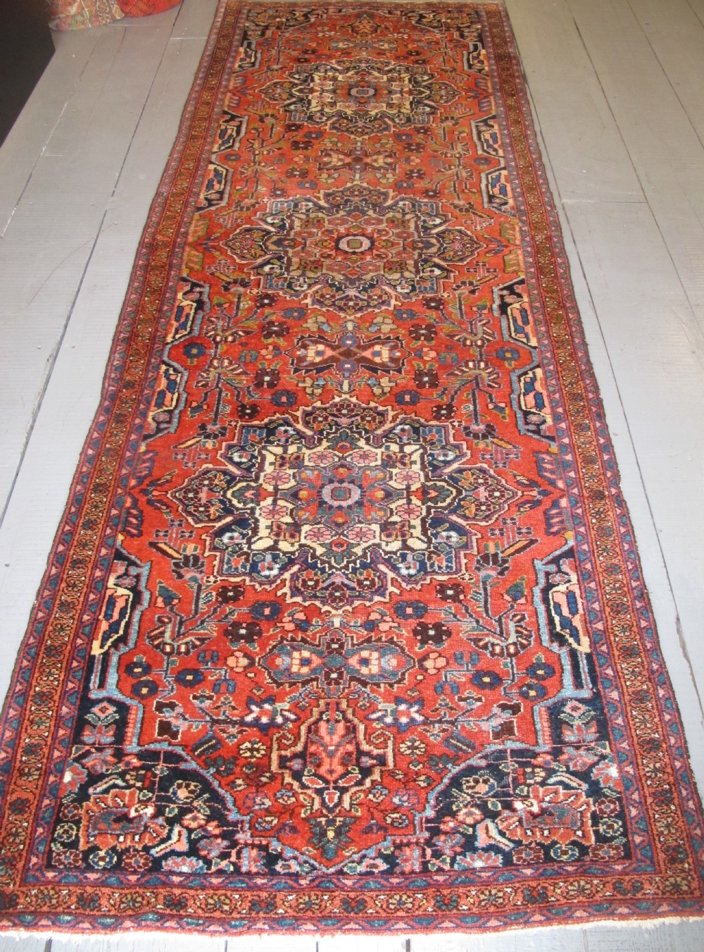A long hand-knotted antique Persian Hamadan runner rug featuring terracotta red, navy blue, and cream floral medallion motifs throughout the central field.