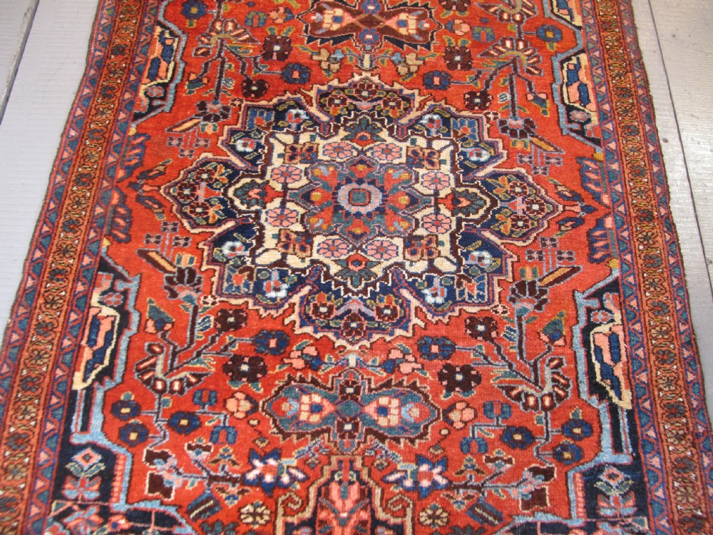 A long hand-knotted antique Persian Hamadan runner rug featuring terracotta red, navy blue, and cream floral medallion motifs throughout the central field. View II