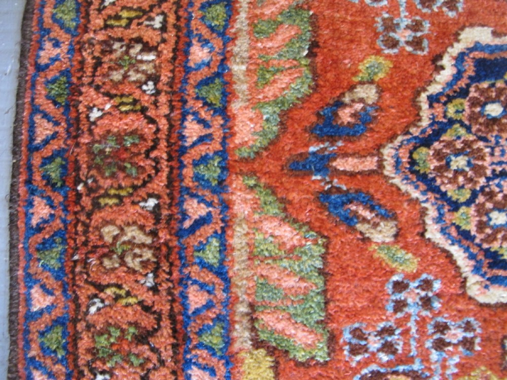 A long hand-knotted antique Persian Hamadan runner rug featuring terracotta red, navy blue, and cream floral medallion motifs throughout the central field. View V