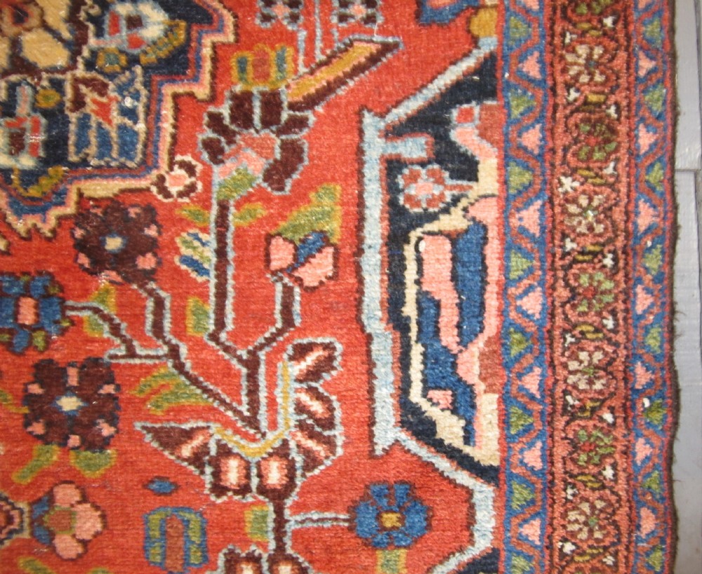 A long hand-knotted antique Persian Hamadan runner rug featuring terracotta red, navy blue, and cream floral medallion motifs throughout the central field. View X