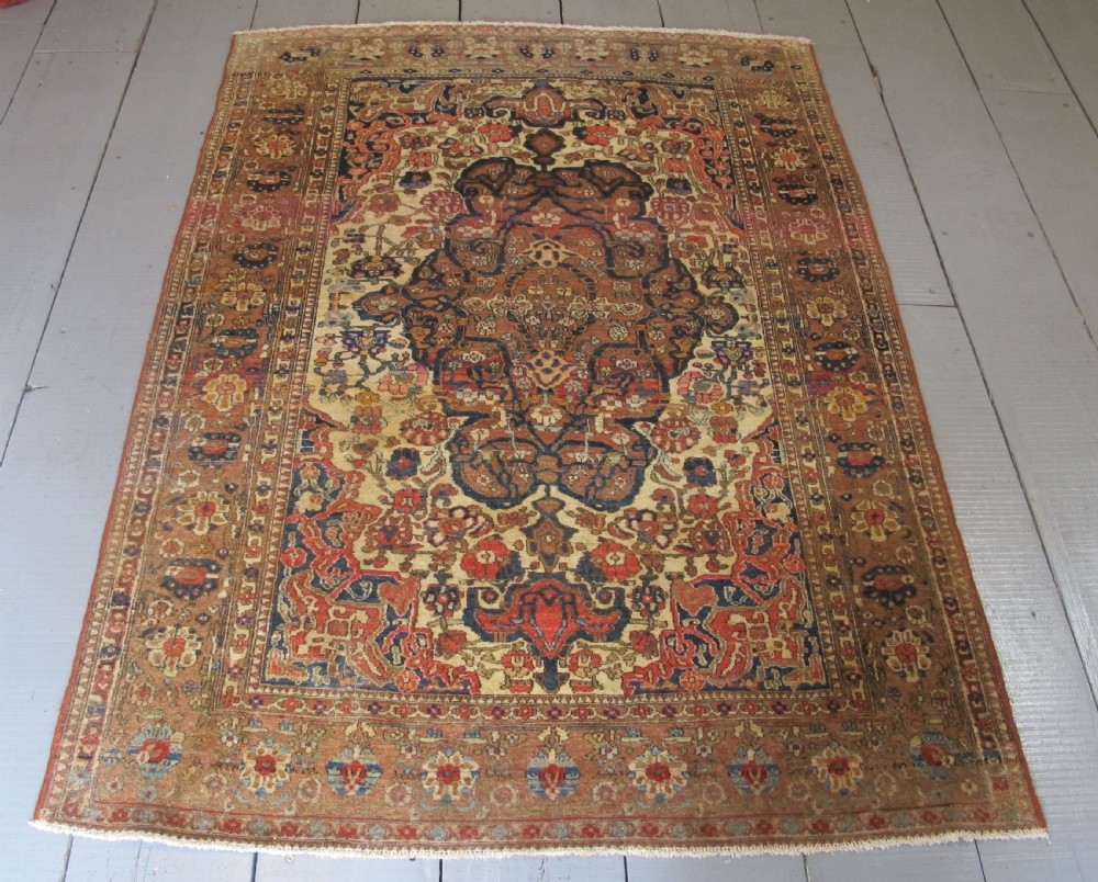 An antique hand-knotted Persian Isfahan area rug featuring an intricate dark blue and terracotta central medallion on an ivory floral field with decorative patterned borders.