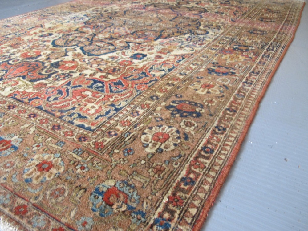 An antique hand-knotted Persian Isfahan area rug featuring an intricate dark blue and terracotta central medallion on an ivory floral field with decorative patterned borders. View IV