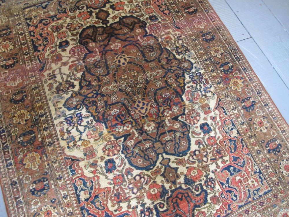 An antique hand-knotted Persian Isfahan area rug featuring an intricate dark blue and terracotta central medallion on an ivory floral field with decorative patterned borders. View V