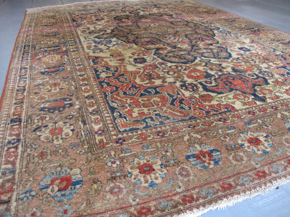 An antique hand-knotted Persian Isfahan area rug featuring an intricate dark blue and terracotta central medallion on an ivory floral field with decorative patterned borders. View VI