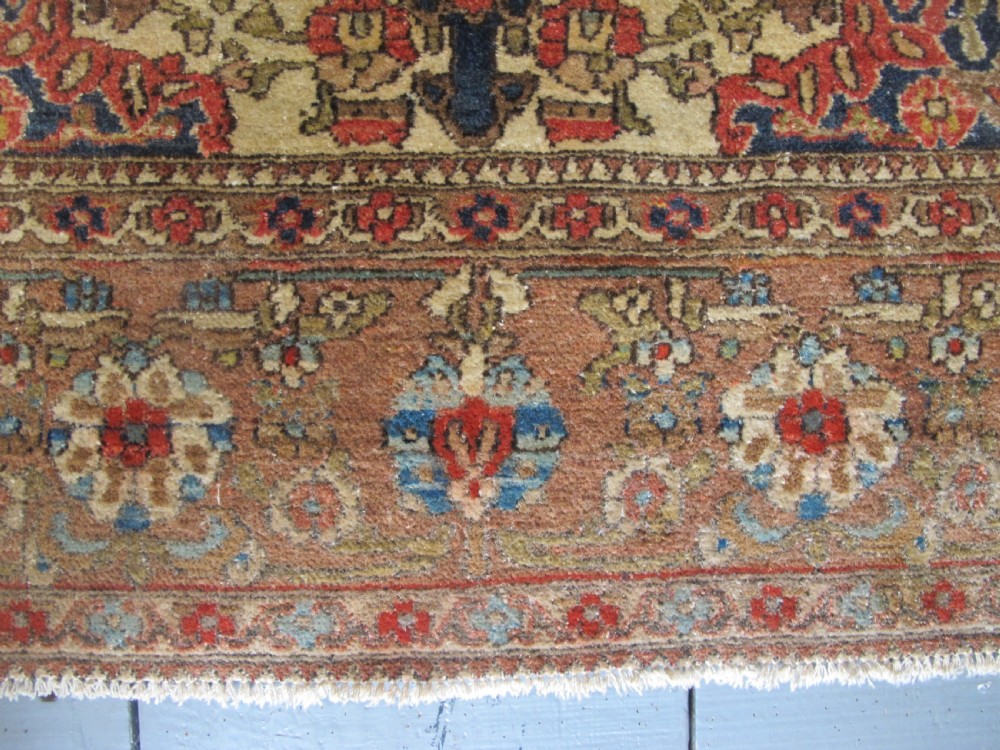 An antique hand-knotted Persian Isfahan area rug featuring an intricate dark blue and terracotta central medallion on an ivory floral field with decorative patterned borders. View VIII
