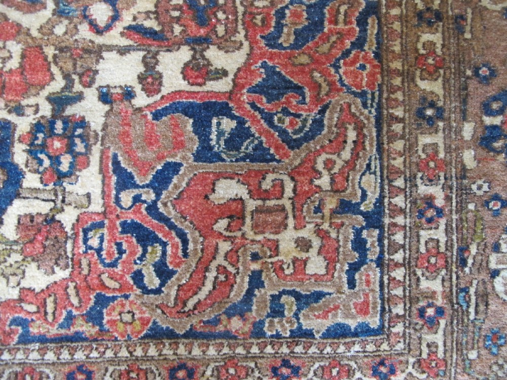 An antique hand-knotted Persian Isfahan area rug featuring an intricate dark blue and terracotta central medallion on an ivory floral field with decorative patterned borders. View X