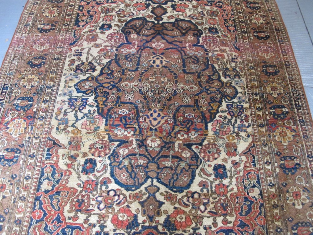 An antique hand-knotted Persian Isfahan area rug featuring an intricate dark blue and terracotta central medallion on an ivory floral field with decorative patterned borders. View XII