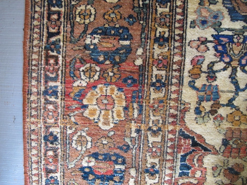 An antique hand-knotted Persian Isfahan area rug featuring an intricate dark blue and terracotta central medallion on an ivory floral field with decorative patterned borders. View XIII