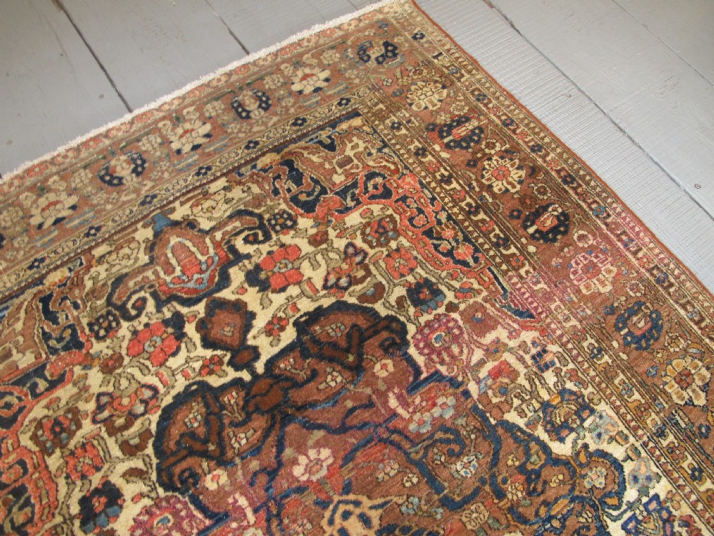 An antique hand-knotted Persian Isfahan area rug featuring an intricate dark blue and terracotta central medallion on an ivory floral field with decorative patterned borders. View XIV