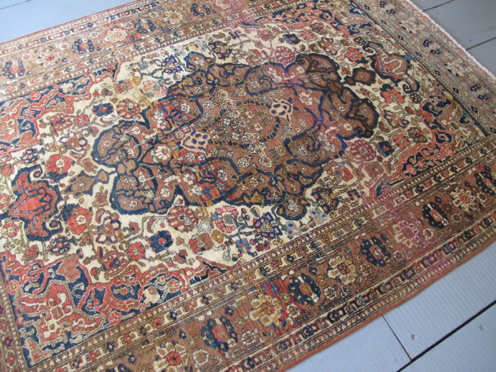 An antique hand-knotted Persian Isfahan area rug featuring an intricate dark blue and terracotta central medallion on an ivory floral field with decorative patterned borders. View XV
