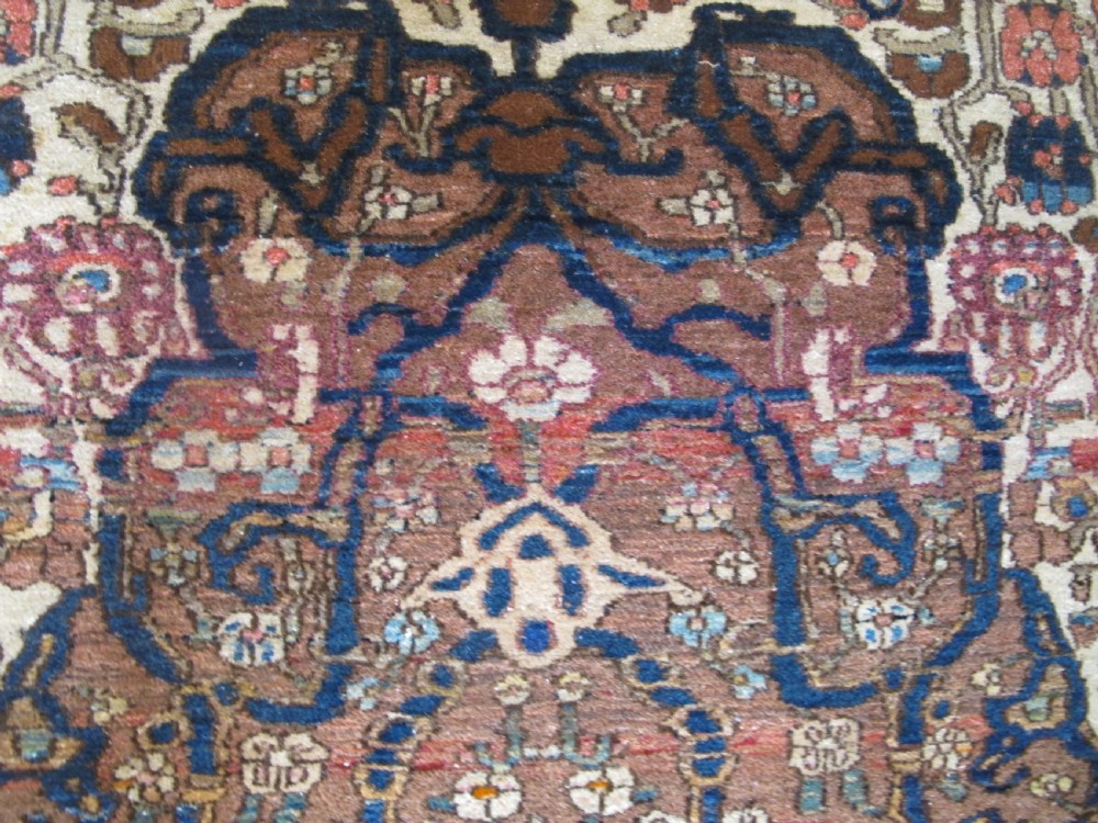 An antique hand-knotted Persian Isfahan area rug featuring an intricate dark blue and terracotta central medallion on an ivory floral field with decorative patterned borders. View XVI