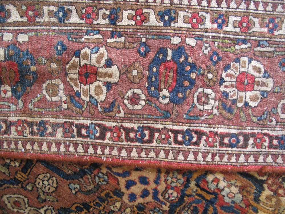 An antique hand-knotted Persian Isfahan area rug featuring an intricate dark blue and terracotta central medallion on an ivory floral field with decorative patterned borders. View XVII