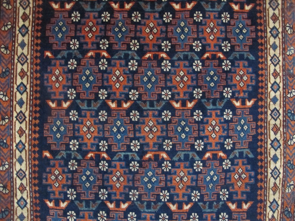 A rectangular hand-knotted wool rug featuring a dark navy central field filled with repeating geometric motifs surrounded by intricate multi-layered pattern borders in blue, terracotta, and cream. View II