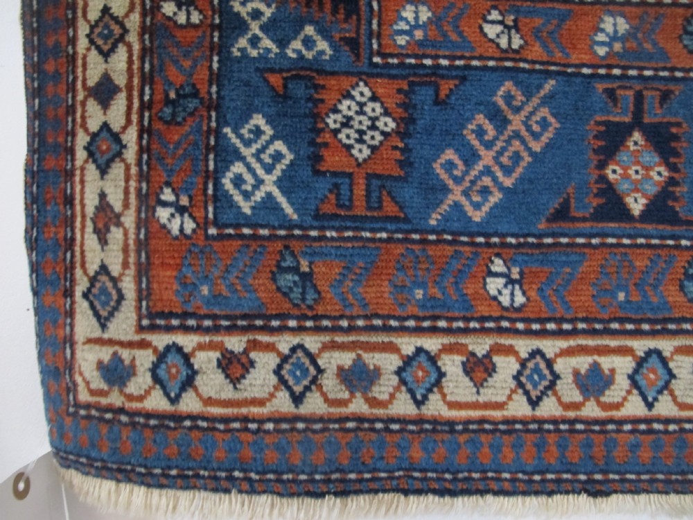 A rectangular hand-knotted wool rug featuring a dark navy central field filled with repeating geometric motifs surrounded by intricate multi-layered pattern borders in blue, terracotta, and cream. View IV