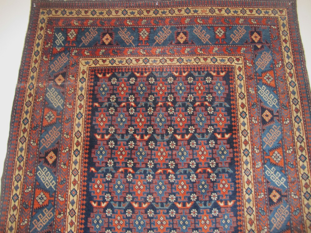 A rectangular hand-knotted wool rug featuring a dark navy central field filled with repeating geometric motifs surrounded by intricate multi-layered pattern borders in blue, terracotta, and cream. View VIII