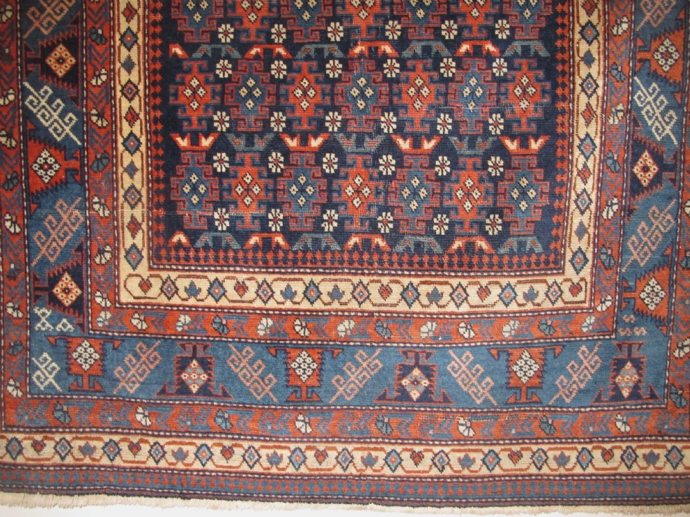 A rectangular hand-knotted wool rug featuring a dark navy central field filled with repeating geometric motifs surrounded by intricate multi-layered pattern borders in blue, terracotta, and cream. View IX