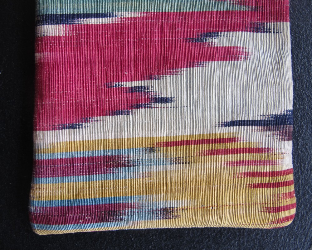 A rectangular double-sided silk ikat purse featuring colourful horizontal bands in pink, yellow, blue, and cream with a red tassel attached at the top opening. View III
