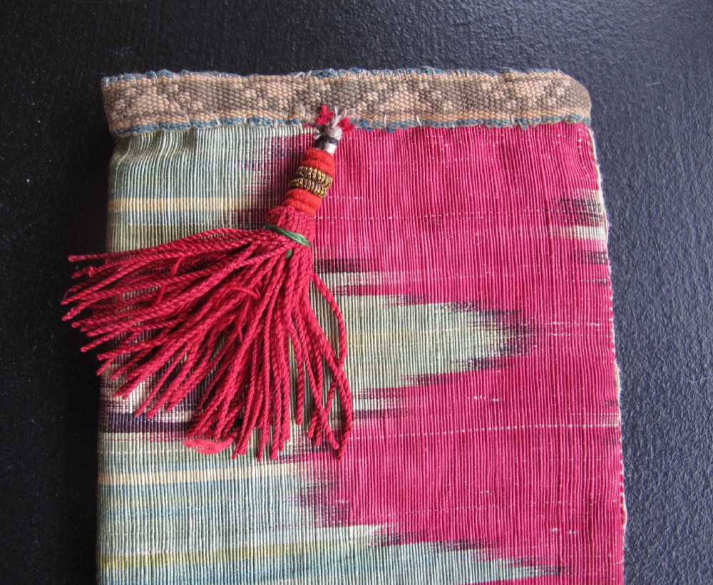 A rectangular double-sided silk ikat purse featuring colourful horizontal bands in pink, yellow, blue, and cream with a red tassel attached at the top opening. View IV