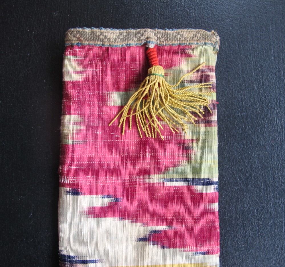 A rectangular double-sided silk ikat purse featuring colourful horizontal bands in pink, yellow, blue, and cream with a red tassel attached at the top opening. View V