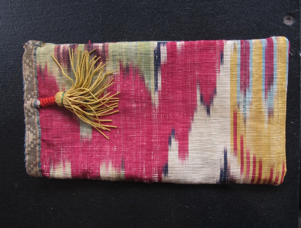 A rectangular double-sided silk ikat purse featuring colourful horizontal bands in pink, yellow, blue, and cream with a red tassel attached at the top opening. View VIII