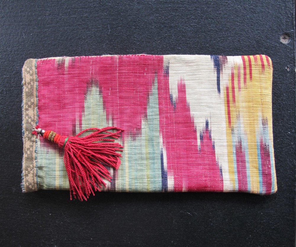 A rectangular double-sided silk ikat purse featuring colourful horizontal bands in pink, yellow, blue, and cream with a red tassel attached at the top opening. View IX