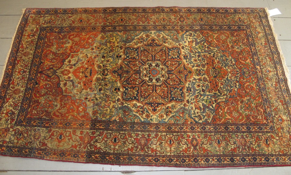 An antique hand-knotted Persian Isfahan rug featuring a central floral medallion surrounded by arabesque scrollwork and detailed multi-banded borders in terracotta red, navy blue, and cream.