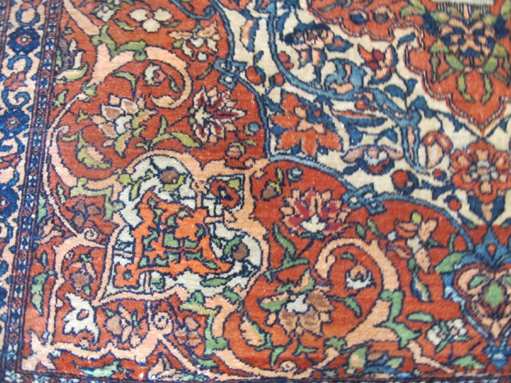 An antique hand-knotted Persian Isfahan rug featuring a central floral medallion surrounded by arabesque scrollwork and detailed multi-banded borders in terracotta red, navy blue, and cream. View V