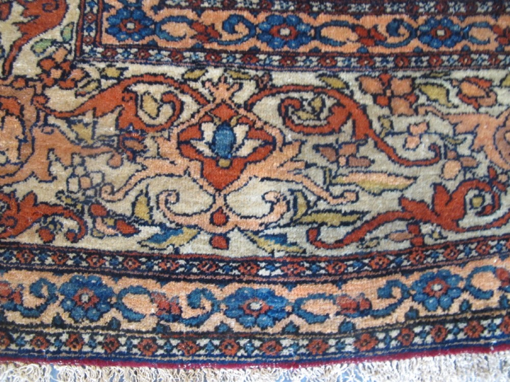 An antique hand-knotted Persian Isfahan rug featuring a central floral medallion surrounded by arabesque scrollwork and detailed multi-banded borders in terracotta red, navy blue, and cream. View VI