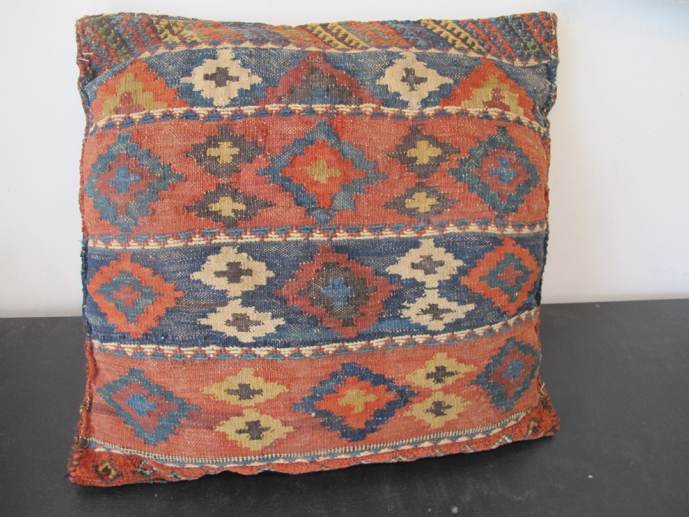 A square handwoven Kurdish wool cushion featuring geometric diamond motifs in blue, terracotta, and brown shades. View IV