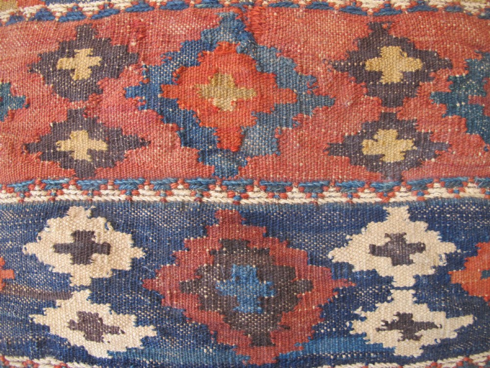 A square handwoven Kurdish wool cushion featuring geometric diamond motifs in blue, terracotta, and brown shades. View V