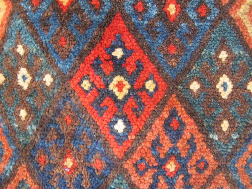 A square handwoven Kurdish wool cushion featuring geometric diamond motifs in blue, terracotta, and brown shades. View IX