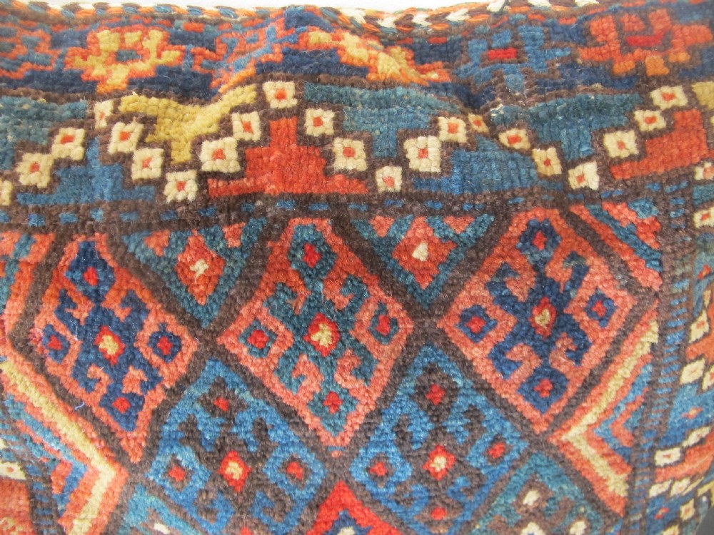 A square handwoven Kurdish wool cushion featuring geometric diamond motifs in blue, terracotta, and brown shades. View X