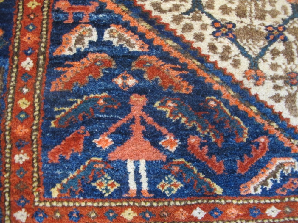 An antique Persian Kolyai hand-knotted wool rug displaying a cream lattice central medallion framed by a deep blue field with stylized figures and tan borders. View II