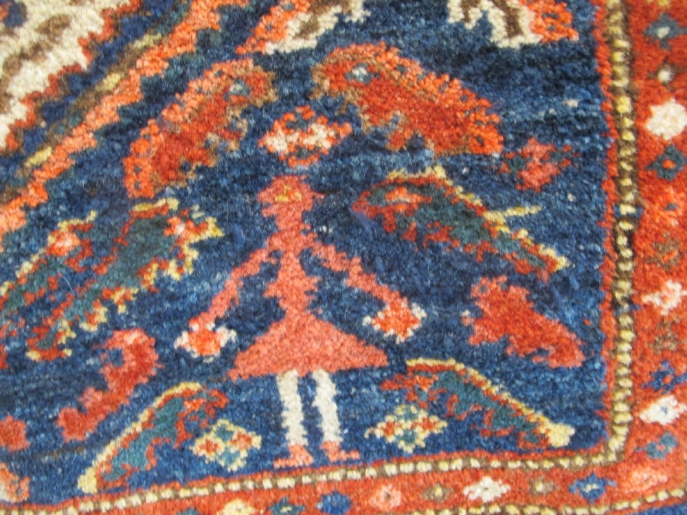 An antique Persian Kolyai hand-knotted wool rug displaying a cream lattice central medallion framed by a deep blue field with stylized figures and tan borders. View III