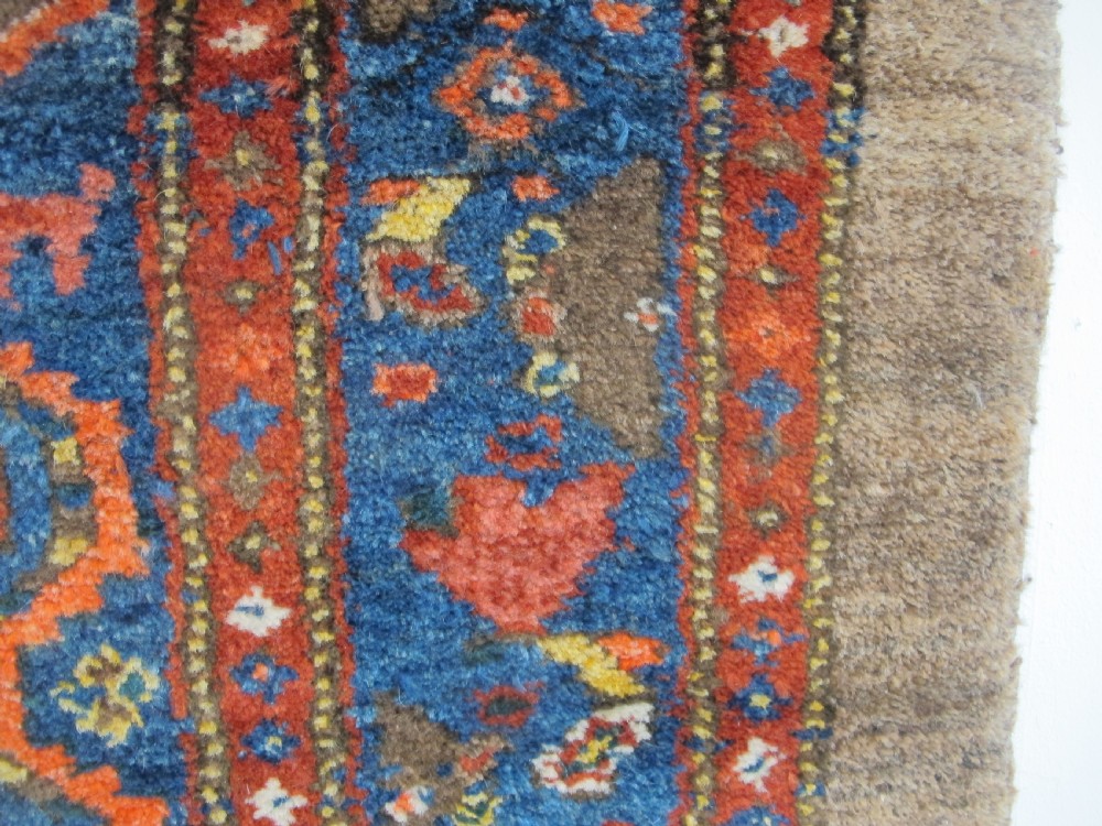 An antique Persian Kolyai hand-knotted wool rug displaying a cream lattice central medallion framed by a deep blue field with stylized figures and tan borders. View IV