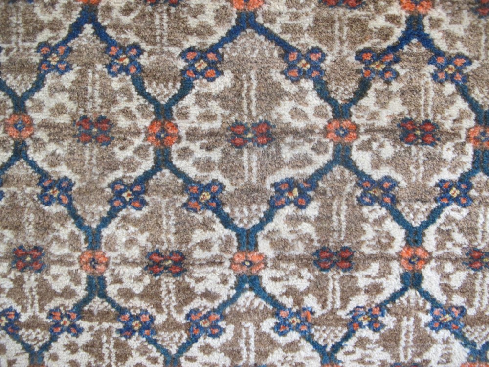 An antique Persian Kolyai hand-knotted wool rug displaying a cream lattice central medallion framed by a deep blue field with stylized figures and tan borders. View V