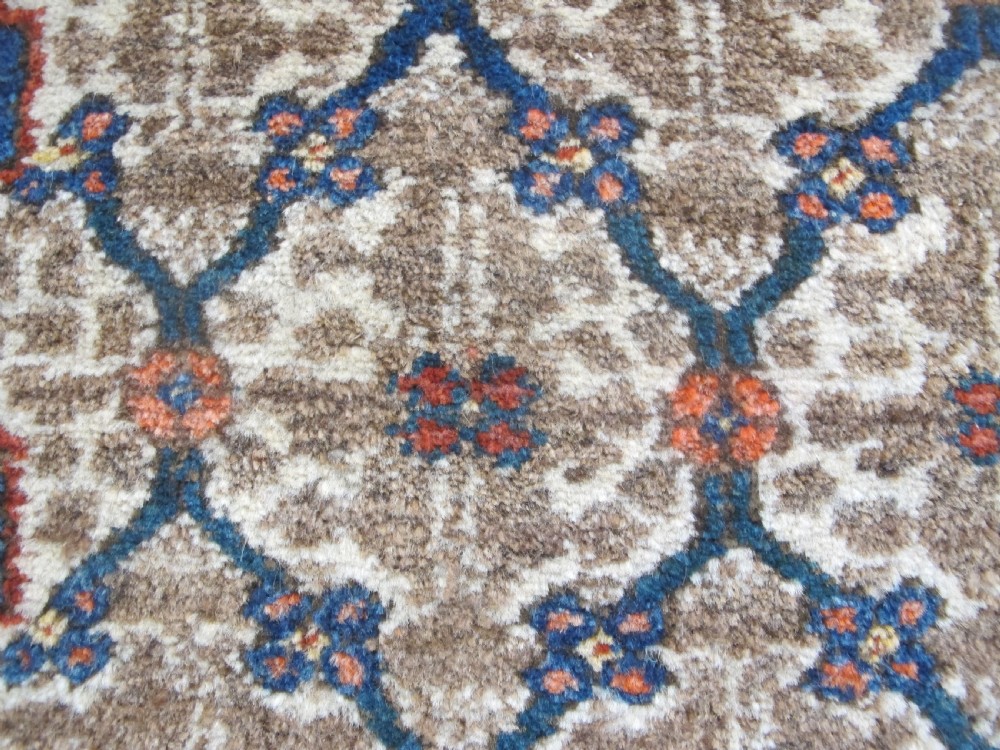 An antique Persian Kolyai hand-knotted wool rug displaying a cream lattice central medallion framed by a deep blue field with stylized figures and tan borders. View VI