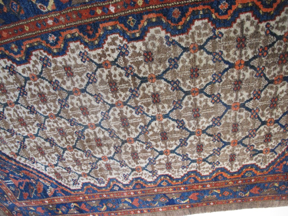 An antique Persian Kolyai hand-knotted wool rug displaying a cream lattice central medallion framed by a deep blue field with stylized figures and tan borders. View VII
