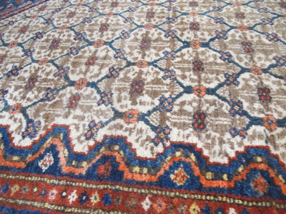 An antique Persian Kolyai hand-knotted wool rug displaying a cream lattice central medallion framed by a deep blue field with stylized figures and tan borders. View VIII