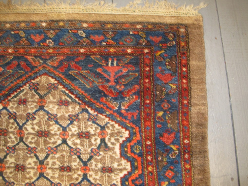 An antique Persian Kolyai hand-knotted wool rug displaying a cream lattice central medallion framed by a deep blue field with stylized figures and tan borders. View XII