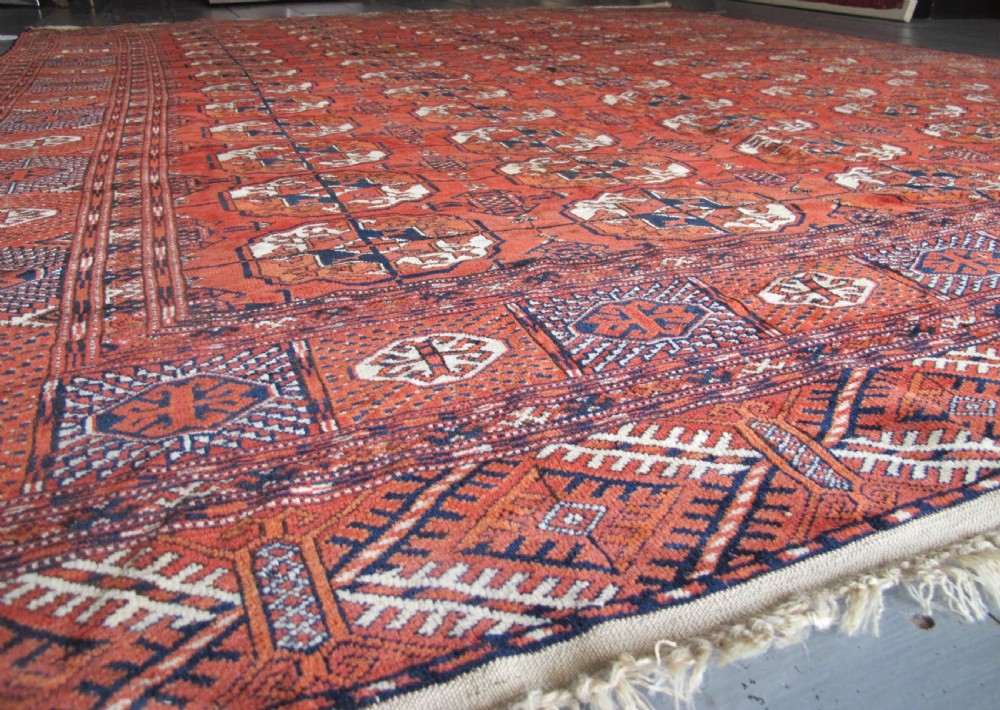 A large hand-knotted antique wool carpet featuring repeating octagonal Tekke gul motifs in rust red, cream, and navy blue with geometric borders. View II