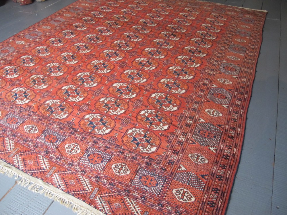 A large hand-knotted antique wool carpet featuring repeating octagonal Tekke gul motifs in rust red, cream, and navy blue with geometric borders. View III