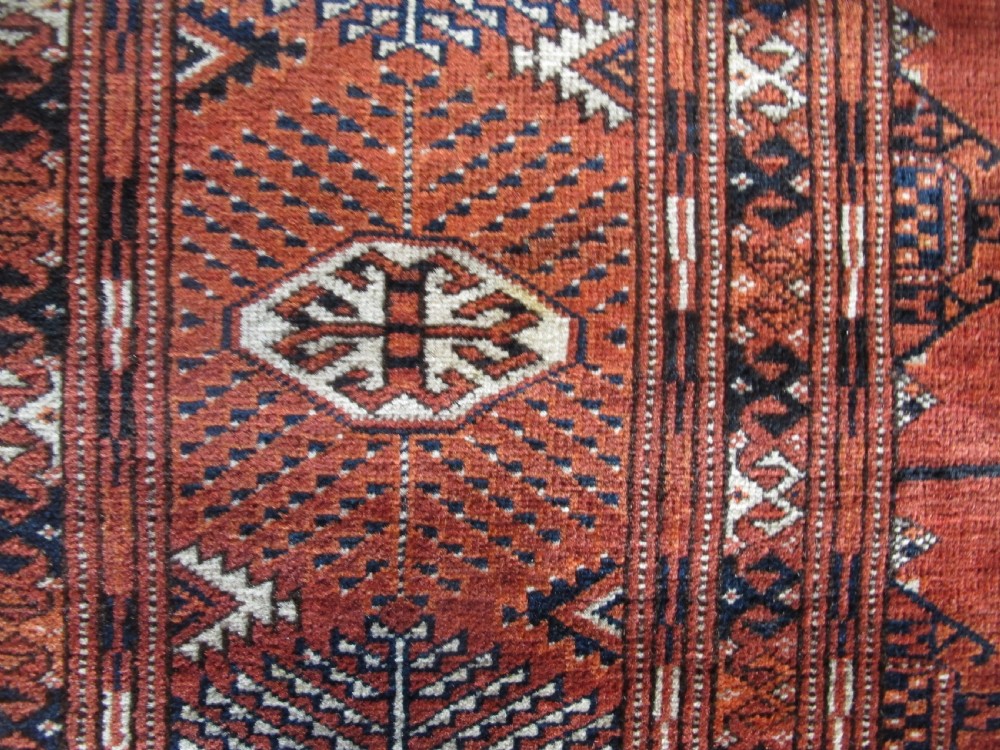 A large hand-knotted antique wool carpet featuring repeating octagonal Tekke gul motifs in rust red, cream, and navy blue with geometric borders. View IX