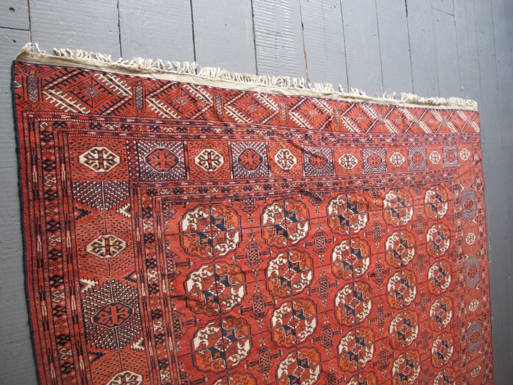 A large hand-knotted antique wool carpet featuring repeating octagonal Tekke gul motifs in rust red, cream, and navy blue with geometric borders. View XI