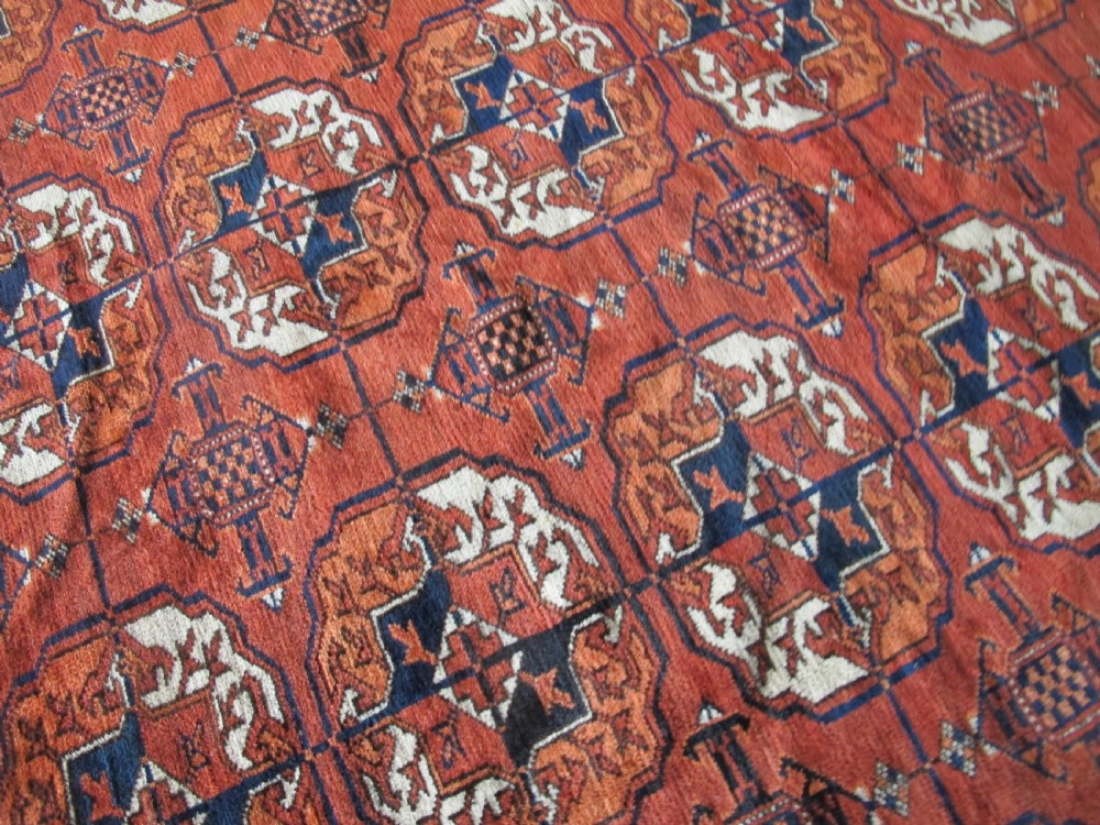 A large hand-knotted antique wool carpet featuring repeating octagonal Tekke gul motifs in rust red, cream, and navy blue with geometric borders. View XIII